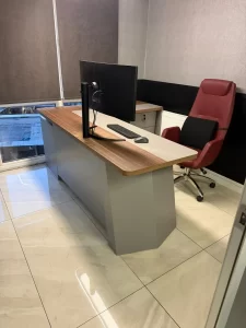 Desk setup with a monitor, keyboard, and mouse on a two-tone desk, and a red ergonomic chair nearby.